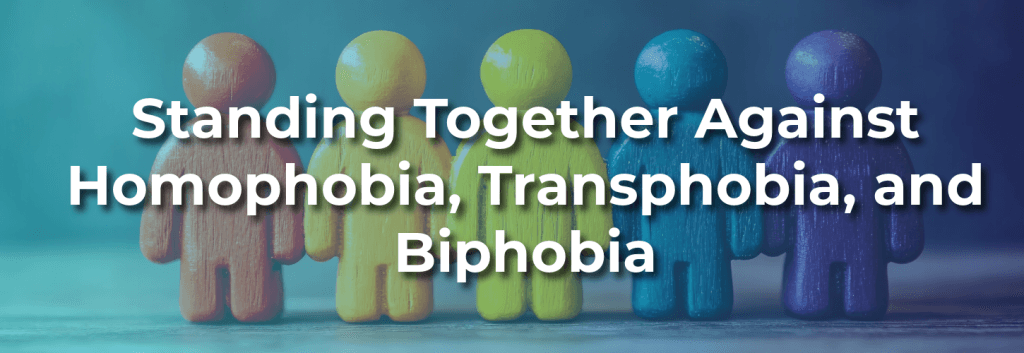 Colorful wooden human figures standing side by side with overlay text reading “Standing Together Against Homophobia, Transphobia, and Biphobia,” representing unity, support, and LGBTQ+ inclusion.