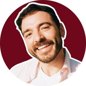 Smiling man with a beard against a burgundy background. He wears a white shirt, radiating happiness and warmth. Casual, friendly tone.